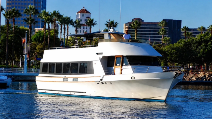 White private party yacht cruising through Long Beach Harbor with palm trees in the background.